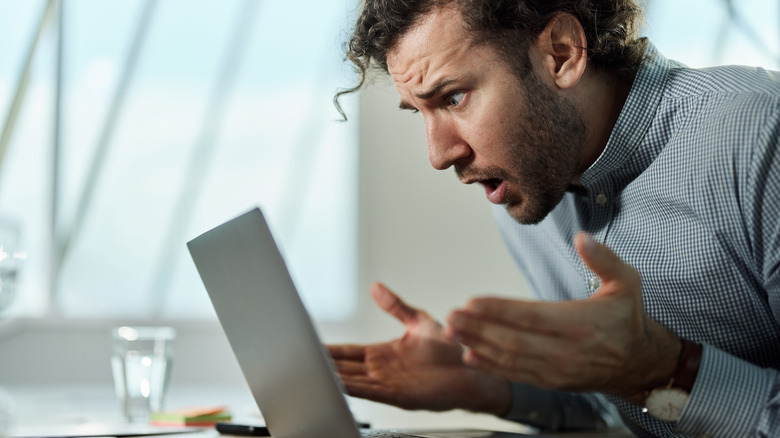 A panicked and shocked man looking at his laptop