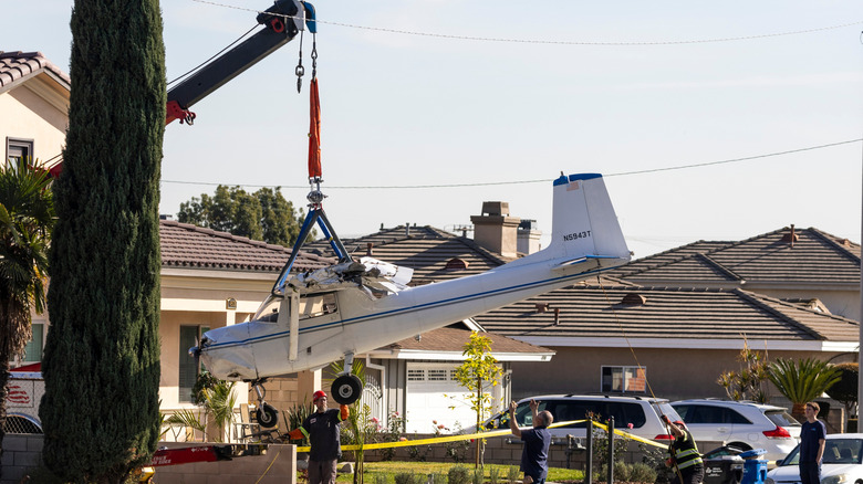 Crane removing small plane from house after crash