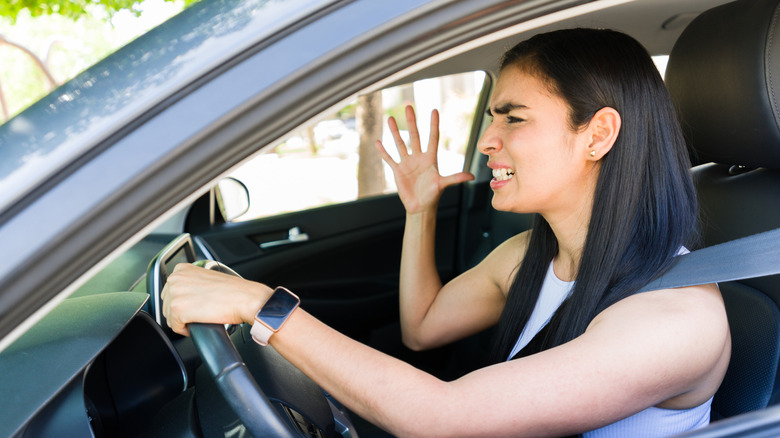 A frustrated woman with long, dark hair behind the wheel of a silver vehicle