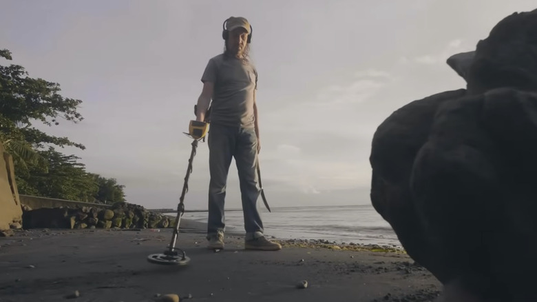 man operates a metal detector on the beach