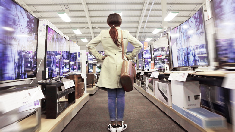 woman standing in an aisle with TVs displayed