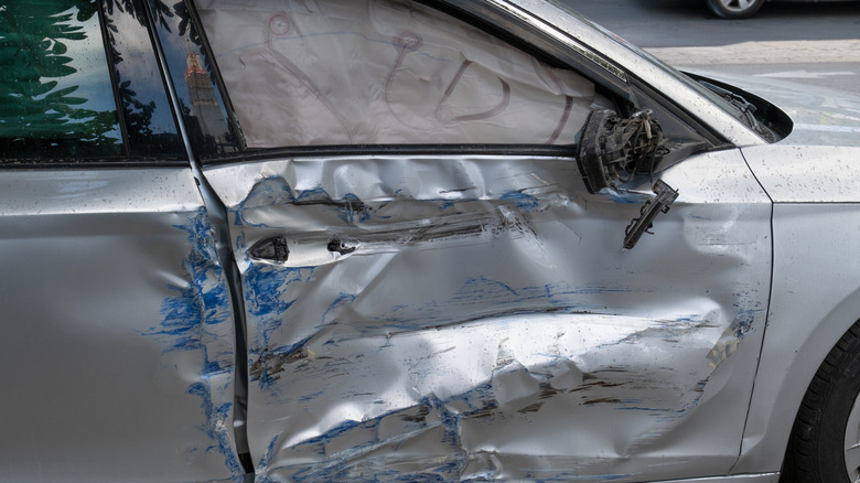 A car with side-impact damage to the door, which deployed the side airbag seen in the broken window.