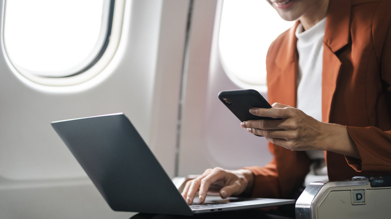 Woman looking at phone and laptop on an airplane