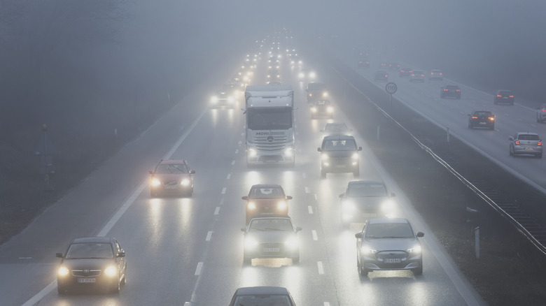 Cars and trucks moving on a highway with headlights on in heavy fog
