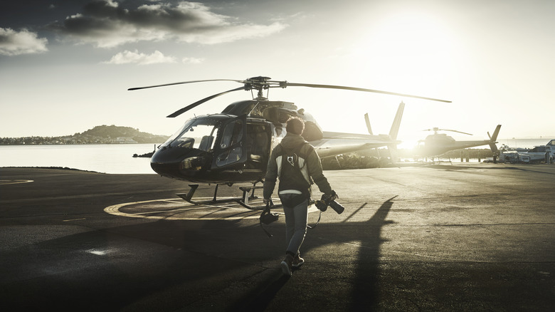 A pilot walks on a helipad toward a grounded black single main rotor helicopter