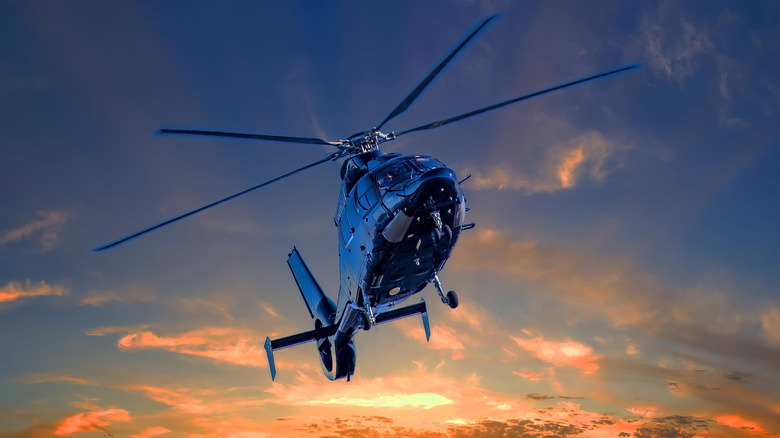 A black single main rotor helicopter flying at sunset