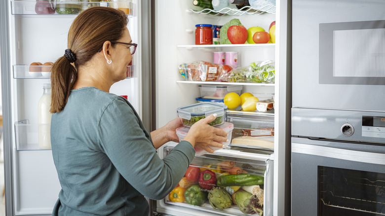 A woman taking food containers out of an open fridge.
