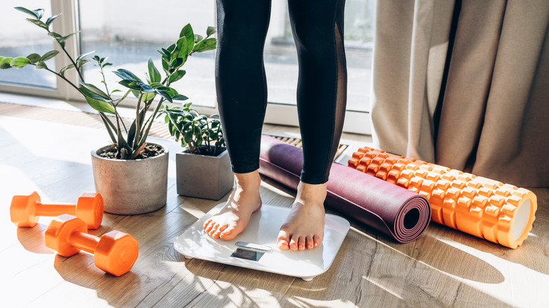Woman standing on a scale with workout equipment nearby
