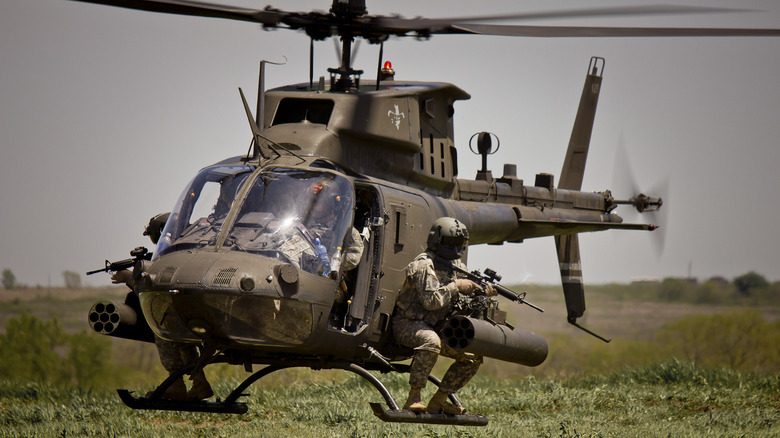 Soldier holding a rifle and sitting on edge of military helicopter