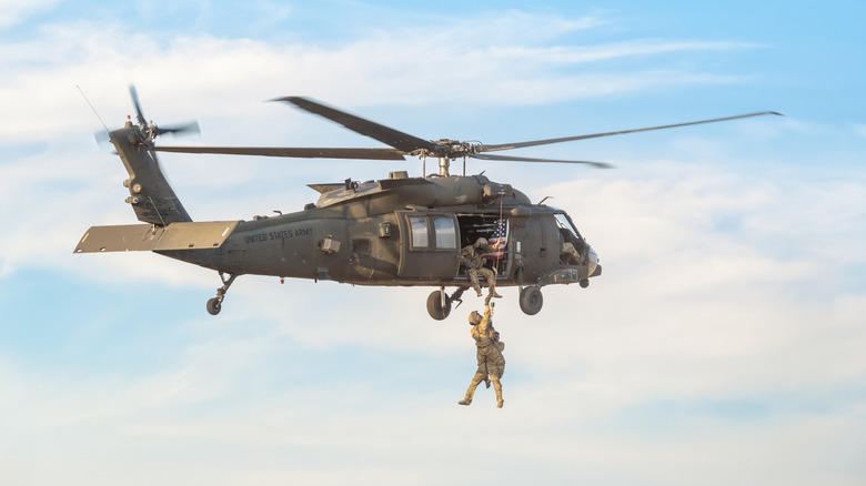 Three soldiers attached to wires on military helicopter