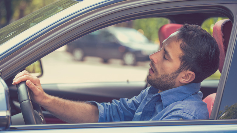 A sleepy, fatigued driver behind the steering wheel of their vehicle with their eyes closed