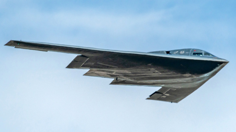 A stealth B-2 bomber is in flight against a cloudy sky backdrop