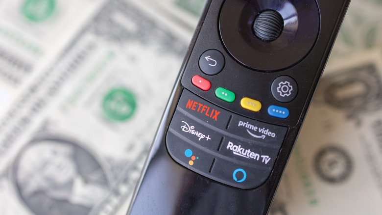 A TV remote shows its Netflix, Prime Video, Disney+, and Rakuten buttons over a pile of money
