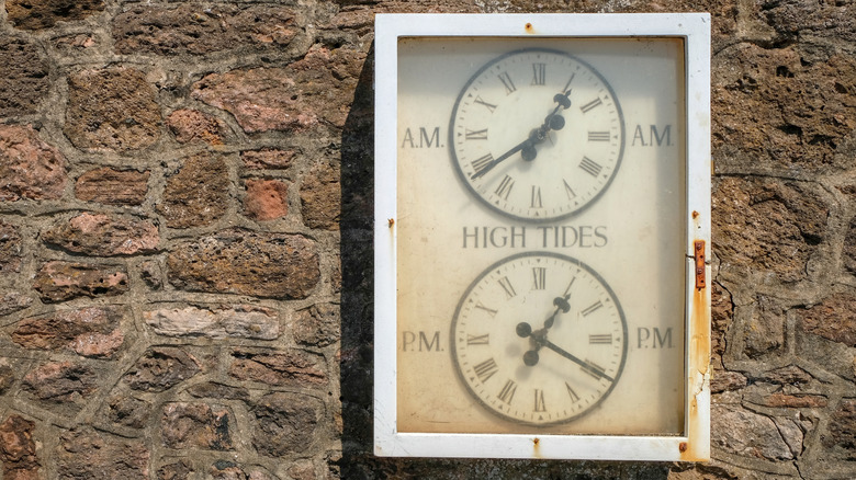 An old, vintage tide clock on a stone wall