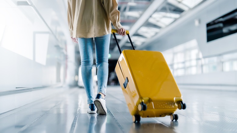 Woman with yellow roller bag walking through an airport