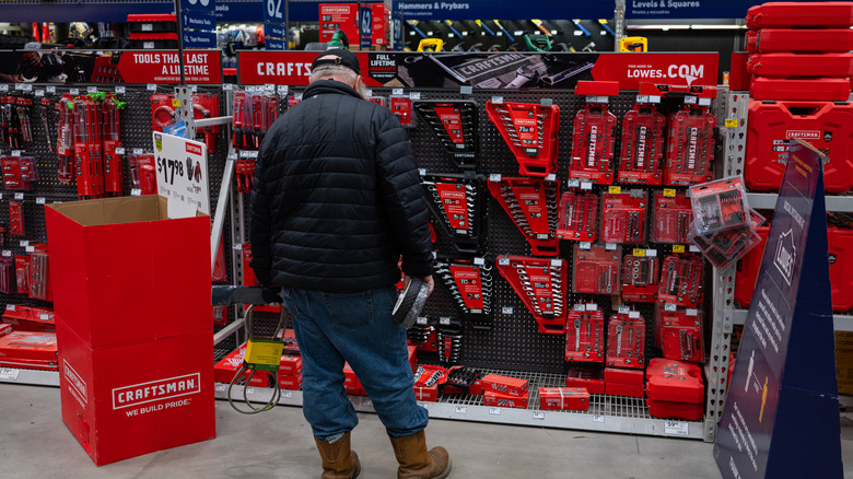 A male shopper in a winter ensemble looking for an item in the tool section of a Lowe's Home Improvement store.