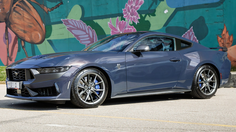 A dark blue Ford Mustang Dark Horse parked in front of a graffiti wall.