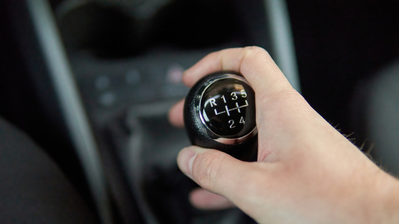 A person holding a manual transmission lever in a car.