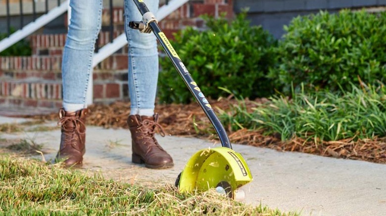Person using Ryobi Expand-It Universal Edger Attachment along walkway
