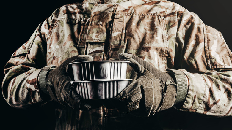 Soldier in camouflaged uniform and tactical gloves holding canned food MRE