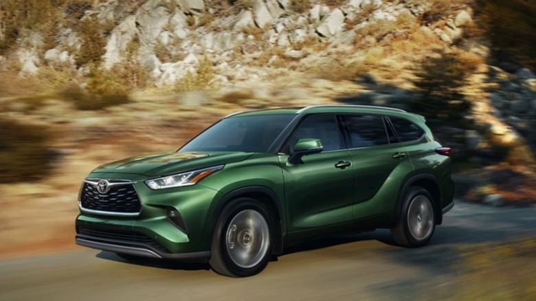 Green Toyota Highlander driving on a road through mountains
