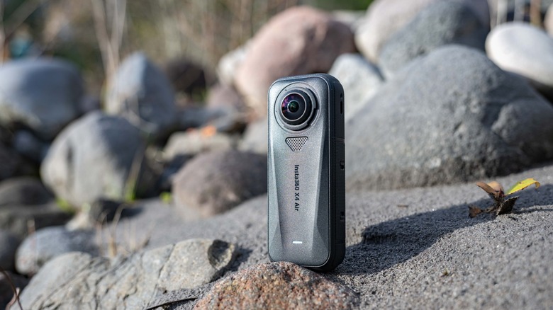 The Insta360 X4 Air standing on sand and rocks.