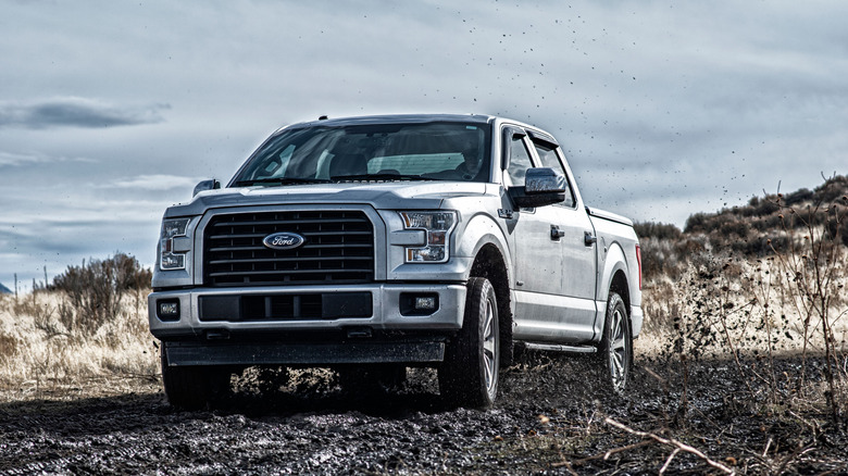 A silver 2015 Ford F-150 kicking up some mud, front 3/4 view