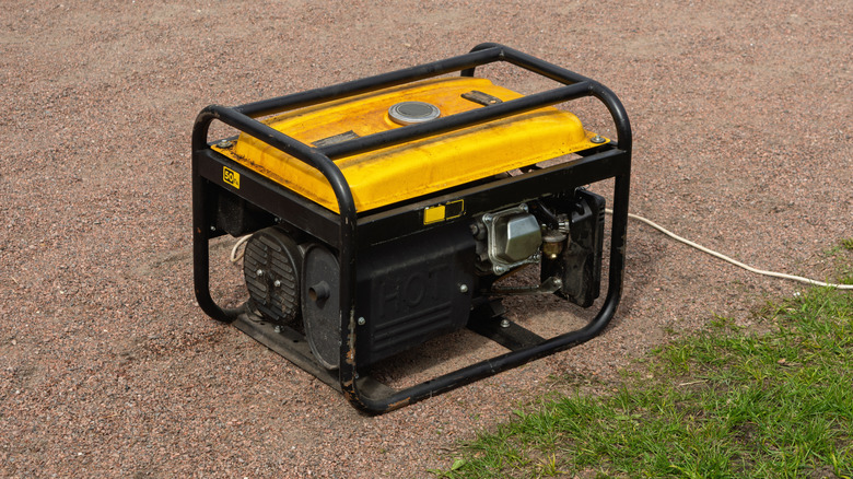 A yellow portable generator sitting in a gravel driveway, with an extension cord plugged into it