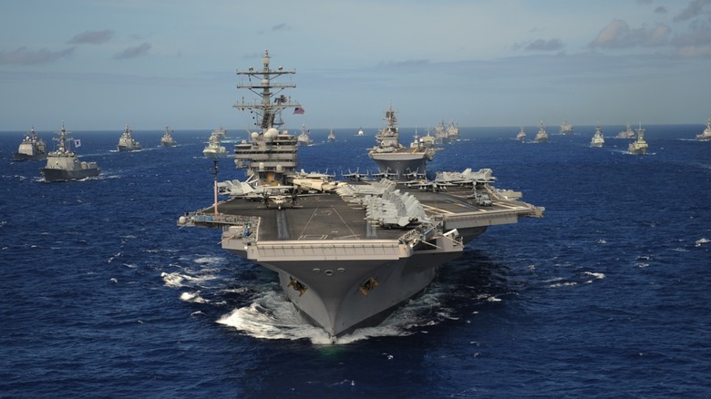 An aircraft carrier at sea with several support ships in the background