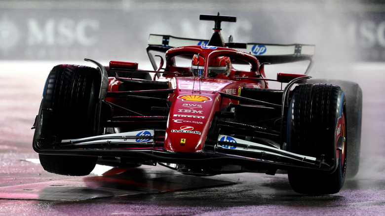 Charles Leclerc driving his Ferrari F1 car over a curb on a wet race track