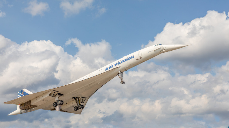 The Concord plane just after take off with a cloudy blue sky behind it.