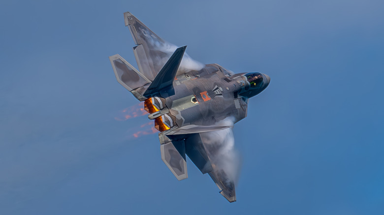 An F-22 flying through a blue sky with its engines alight