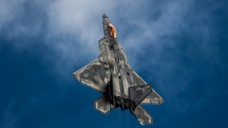 An F-22 Raptor climbs into the clouds on a bright day