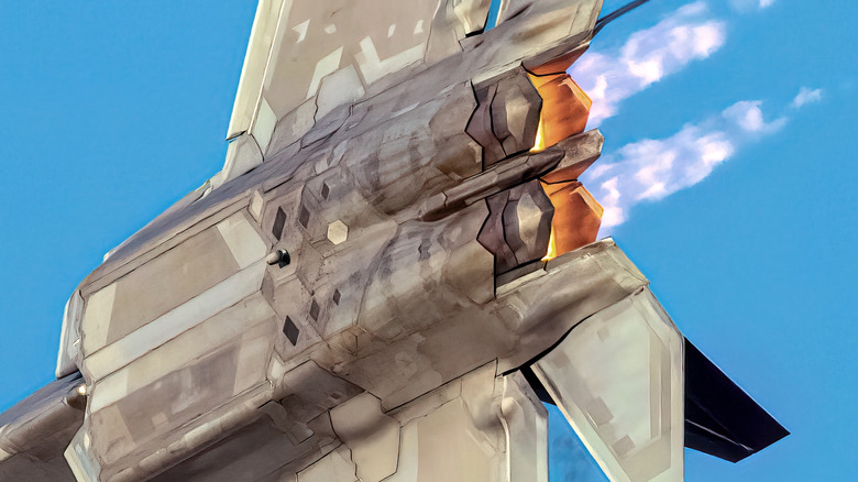 A close-up of an airborne F-22's underside and F119 engines against a blue sky