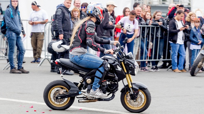 A woman riding a Honda Grom with an audience in the background