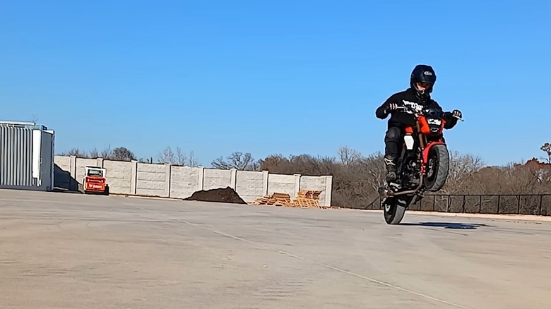 A rider performing a wheelie on a Honda Grom in a parking lot