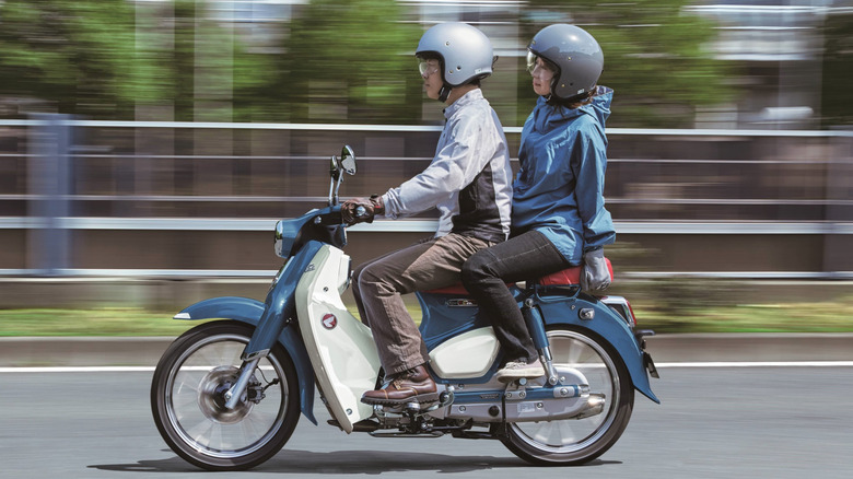 Two people riding Honda Super Cub C125 cruising down the road