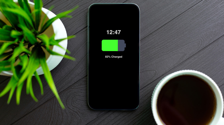 Phone with charged battery on screen background wooden table in cafe