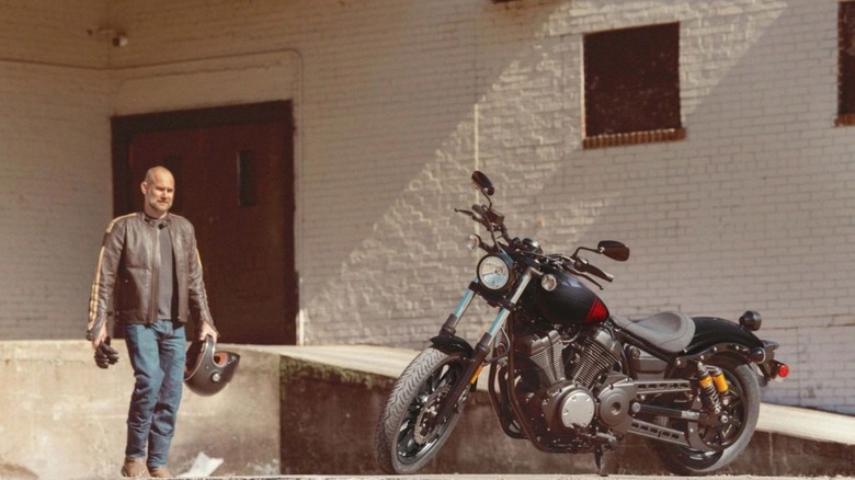 A man approaching a parked Yamaha R-Spec beside a white building