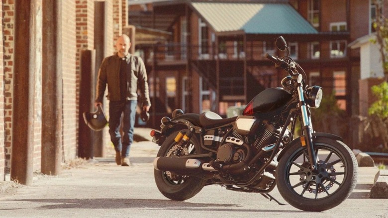 A man walking toward a parked Yamaha R-Spec on a sunny day