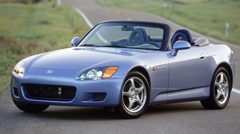 A light blue AP1 Honda S2000 on an empty road, front 3/4 view, roof down
