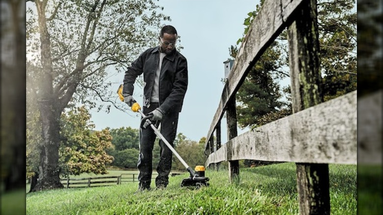 A Man Using A DeWalt 20V 13-Inch String Trimmer Along A Fence