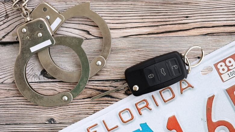 A car key fob, Florida license plate, and handcuffs on a wood surface.