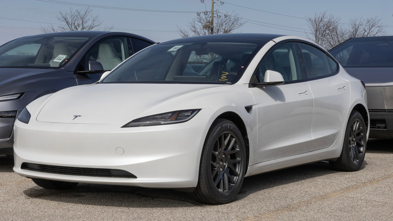 A white Tesla Model 3 parked at a dealership lot.
