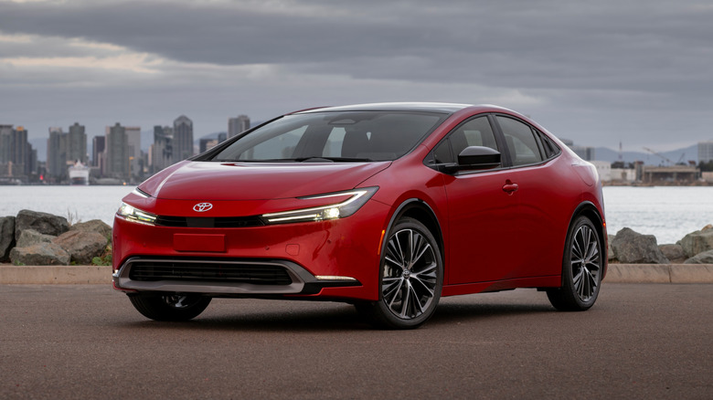 Supersonic Red 2023 Toyota Prius XLE parked on a paved surface with a body of water and cityscape in the background