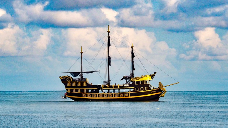 Black and gold galleon sailing on calm seas with a cloudy sky overhead
