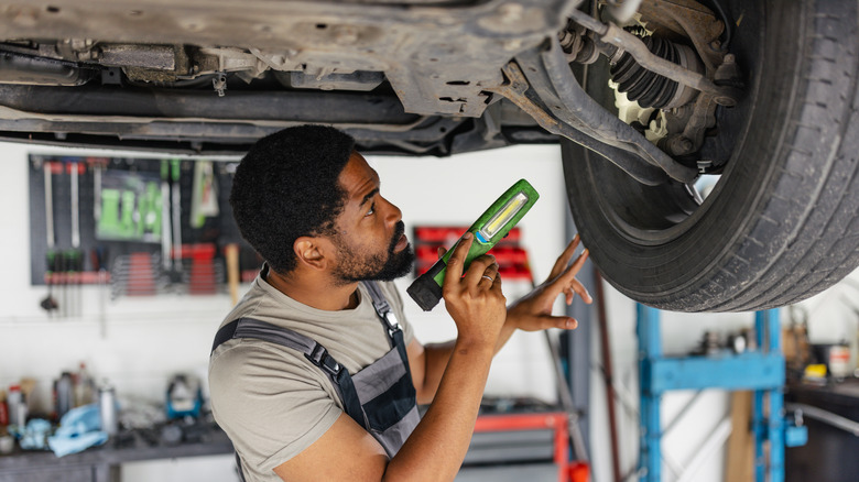 Mechanic servicing front-end of car on a lift while holding light