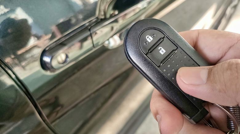 A close-up of a hand holding a car fob next to a black vehicle