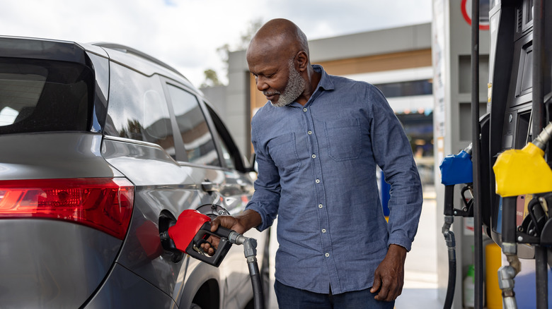 African American senior man refueling his car at a gas station and holding the pump