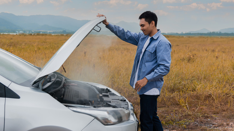A man standing over an overheated engine with steam rising up